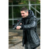 A man wearing a black leather hooded jacket with faux-fur trim and a black hoodie, holding a rifle in an outdoor setting.