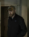 Man wearing a cap and black jacket with Patagonia logo in a dimly lit room.