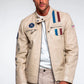 Man wearing a beige jacket with patches on a plain background
