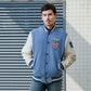 Man wearing a blue and white letterman jacket with USA emblem against a tiled wall.