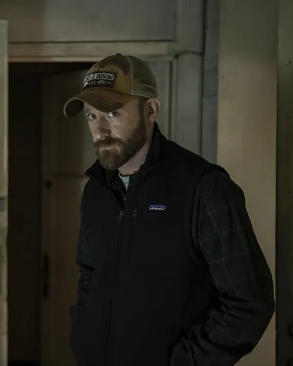 Man wearing a cap and black jacket with Patagonia logo in a dimly lit room.