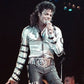 Person in a silver jacket with reflective material on stage holding a microphone.
