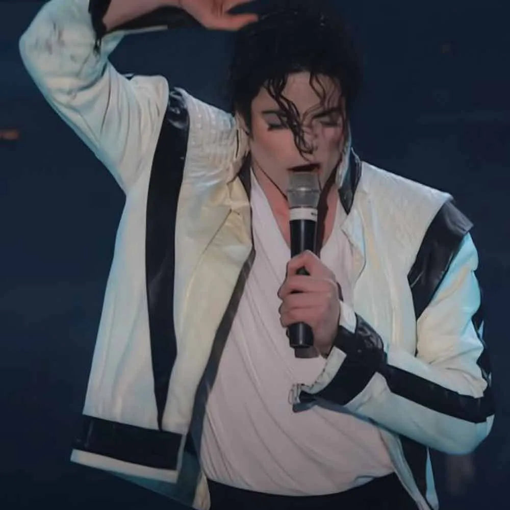 Person in a white and black jacket holding a microphone against a dark background