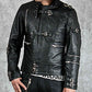 Person wearing a black leather jacket with metallic accents on a gray background