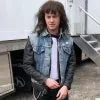 Person wearing a denim vest and holding a guitar outdoors