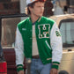 Person wearing a green and red letterman jacket with a logo, standing next to a vintage car.