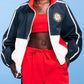 Person wearing a navy, red, and white tracksuit with a blue background