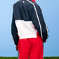 Person wearing a navy, white, and red tracksuit against a blue sky.