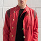 Person wearing a red jacket with gold accents against a gray brick wall.
