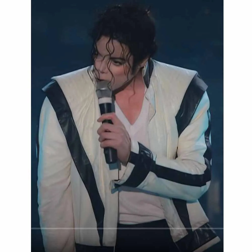 Person wearing a white jacket with black accents, holding a microphone against a dark background