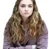 Person with long hair wearing a purple shirt against a plain background