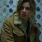 Woman wearing a brown jacket with fur lining in front of a wall with shell patterns
