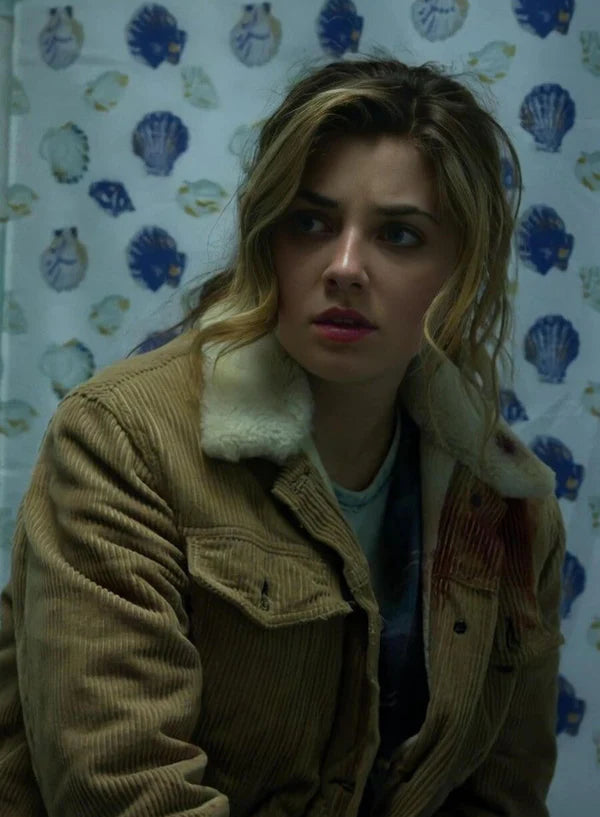 Woman wearing a brown jacket with fur lining in front of a wall with shell patterns